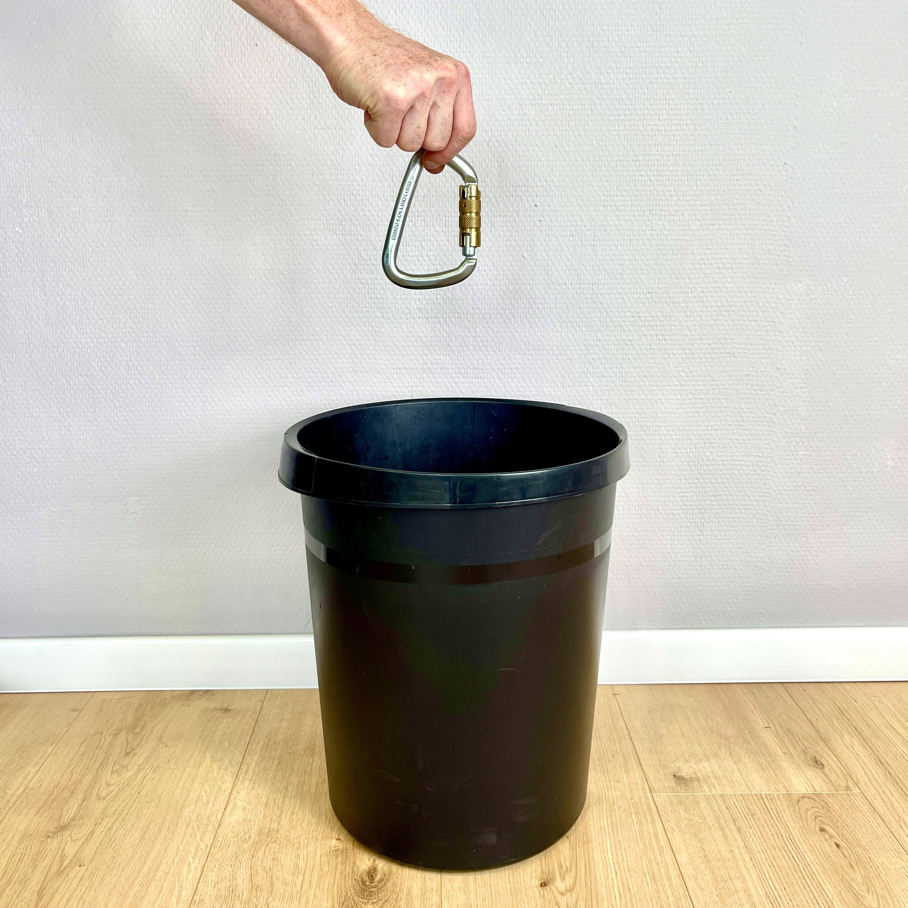 Eine Hand hält einen Karabiner über einem Mülleimer.